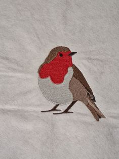 a small bird with a red breast on a white t - shirt that is embroidered onto it