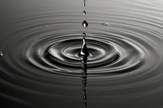 a black and white photo of water ripples in the middle of the image, with one drop falling into the water