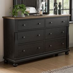 a black dresser with several vases on top of it and a bed in the background