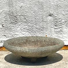 a stone bowl sitting on top of a cement floor next to a white stucco wall