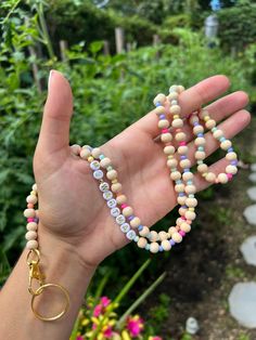 a person holding two bracelets in their hand with flowers and bushes in the background