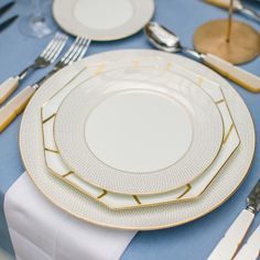 the table is set with white and gold plates, silverware, and napkins