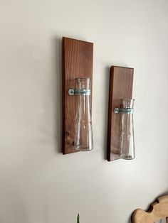 two glass vases are mounted on the wall next to a wooden shelf with a plant in it