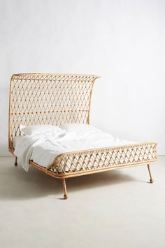 a bamboo bed frame with white sheets and pillows on the bottom, in front of a plain wall