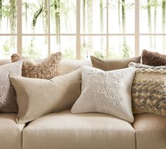 a couch with many pillows on it in front of a window and some trees outside