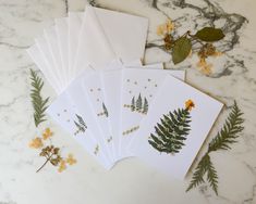 five cards with plants and leaves on them sitting on a marble table next to flowers