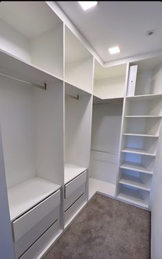 an empty walk in closet with white shelves and shelving units on the wall, carpeted floor