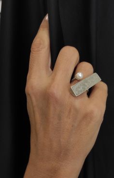 "The sterling silver bar concrete ring is a striking and modern piece of jewelry that combines silver, concrete, and a beautiful freshwater pearl. Handcrafted with precision and attention to detail, this architectural geometric ring features a semi-circular bar inlaid with concrete. Adding a touch of elegance, a round freshwater pearl adorns  of the bar, creating a stunning contrast against the concrete. With its minimalist design and unique materials, this ring is versatile enough to be worn both as an everyday accessory and for special occasions. This statement ring is sure to catch the eye and complete your look perfectly. DESCRIPTIONS and MEASUREMENTS: Materials: Sterling silver and dark grey concrete . Gemstone : Freshwater pearl 0,6x0,65 (cm) 0,23x0,25\" (in) Bar dimensions: 3,7x1,0 Circular Bar, Cement Jewelry, Concrete Ring, Concrete Jewelry, Contemporary Ring, Geometric Ring, Silver Bar, Modern Ring, Silver Jewelry Rings