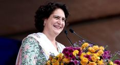 a woman standing at a podium with flowers in front of her and holding a microphone