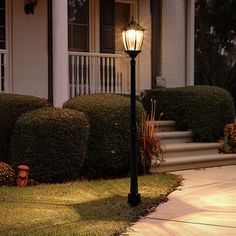 a lamp post in front of a house with grass and bushes on the side walk