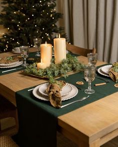 the table is set for christmas dinner with candles and greenery on it's placemats