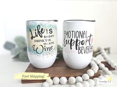 two coffee mugs sitting on top of a wooden table next to white beads and greenery