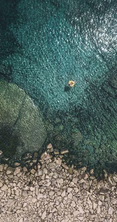 an aerial view of rocks and water with a boat in the middle one is yellow