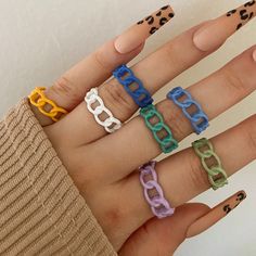 a person's hand with five different colored rings on their fingers and one is wearing leopard print nail polish