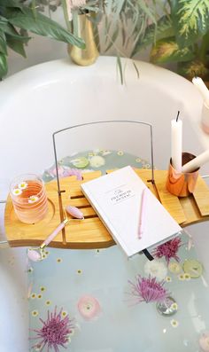 a bath tub with a book, pen and candle holder on the tray next to it