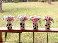 four vases with pink and white flowers are on a wooden ledge near a grassy field