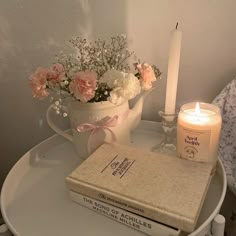 a candle, book and flowers are on a small white table with a flower pot