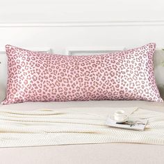 a pink leopard print pillow sitting on top of a bed next to a white blanket