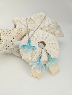 two blue and white necklaces sitting on top of a piece of driftwood next to a sea urchin