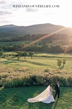 a bride and groom walking in the grass with mountains in the background at their wedding