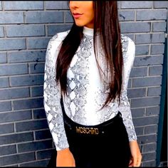 a woman standing in front of a brick wall wearing a white shirt and black pants