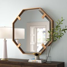 a mirror sitting on top of a wooden dresser next to a lamp and a potted plant