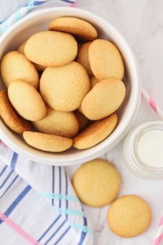 a white bowl filled with cookies next to a glass of milk on top of a blue and white towel