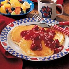 a plate with pancakes covered in sauce next to a bowl of fruit and a cup of coffee