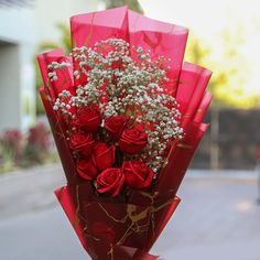 a bouquet of red roses and baby's breath wrapped in red paper on the street