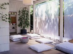 a room that has some white pillows on the floor and plants in the corner behind it