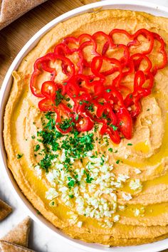 hummus with red peppers and parsley in a white bowl