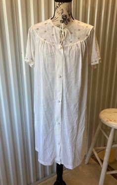 This sweet late 1960s/early 1970s nylon robe or nightgown by Komar is soft and feels like wearing a cloud. White nylon, a button- and tie-front closure, little embroidered flowers decorate the top. I believe it was the robe to a set due to the fabric covered buttons, but could be worn as either a robe or a nightgown. Measurements, lay flat unless otherwise stated: Pit to pit measurement is 20" Waist 24" Hips 24" Overall length is 39" Shoulder to shoulder is 16" Sleeves are 8 1/2" long Armhole opening is 8"