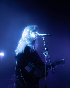 a woman singing into a microphone while holding a guitar