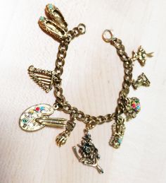 "EASY LAYAWAY IS AVAILABLE A very pretty vintage charm bracelet with 9 intricately formed charms many of them \"jeweled\". Dark gold-tone bracelet consisting of ballerina on tiptoes with 1 tiny pearl missing 2 , ice skater's shoe, jeweled telephone, jeweled golf bag with sticks may be missing one tiny pearl on one side, wishbone with flower may have been a tiny jewel in flower, ornate vintage hand may have held tiny jewel, jeweled painter's palette, jeweled ballerina shoes, harp may or may not b Themed Multicolor Craft Supplies For Gifts, Vintage Handmade Craft Supplies, Vintage Handmade Craft Supplies For Gifts, Handmade Themed Craft Supplies For Gifts, Themed Handmade Craft Supplies For Gifts, Skater Shoes, Painters Palette, Vintage Charm Bracelet, Ice Skaters