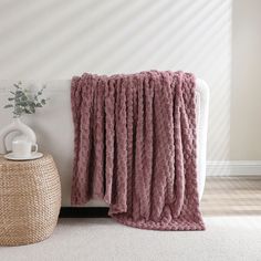 a pink blanket sitting on top of a white couch next to a vase with flowers