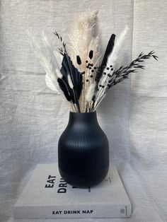 a black vase filled with feathers on top of a book