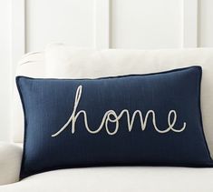 a blue pillow with the word home on it sitting on a white couch in front of a window