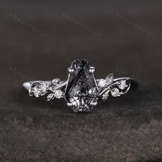 a black diamond ring on top of a stone slab with leaves and vines around it