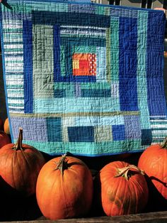 some pumpkins are sitting on a wooden table with a quilted square in the middle