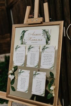 a wooden easer with seating cards attached to it and greenery on the side