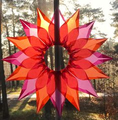 an orange and pink paper sunflower sitting on top of a pole in front of trees