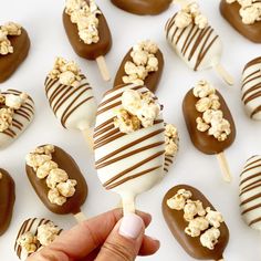 a hand holding a chocolate covered marshmallow lollipop with caramel and popcorn on it