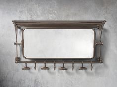 a mirror mounted to the side of a wall with hooks on it and an empty shelf below