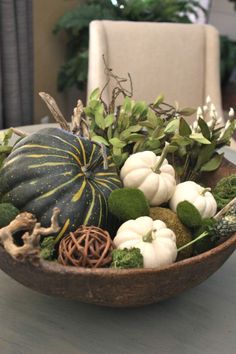 a wooden bowl filled with white pumpkins and greenery on top of a table