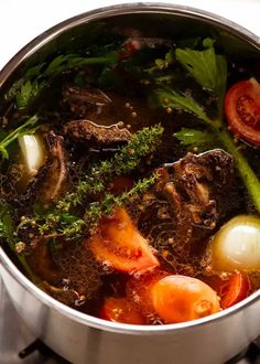 a pot filled with meat and vegetables on top of a stove burner next to tomatoes