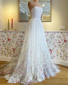 a wedding dress on display in front of a wallpapered room with a mirror