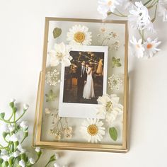 a photo frame with white flowers and greenery on the table next to it is an image of a bride and groom