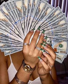 a woman holding money in her hands while wearing green nail polish and ring bracelets