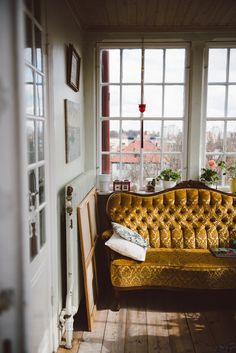 a yellow couch sitting in front of a window next to a wooden floor and white walls