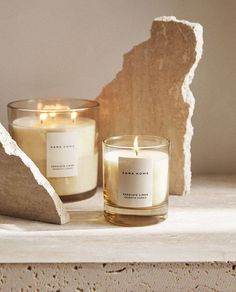 two candles sitting on top of a table next to a piece of driftwood and a rock